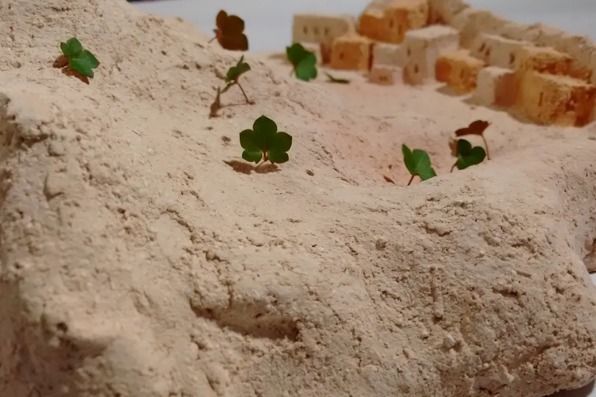 Pequeñas hojas sobre un paisaje de cerámica que representan a personas migrantes.